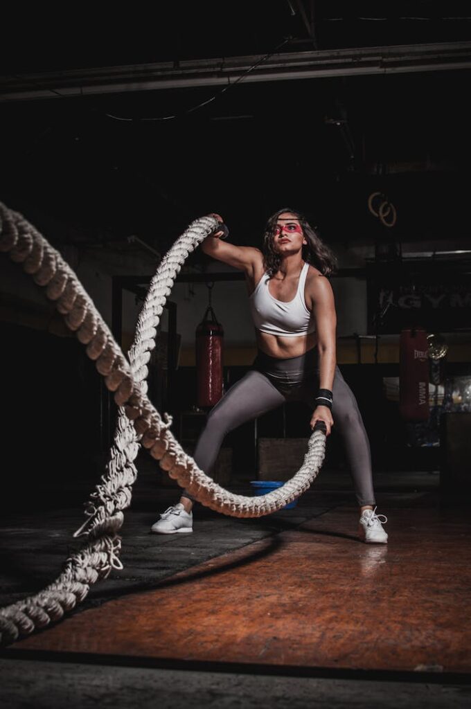 Female athlete demonstrating strength with battle ropes in a gym.